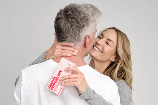 Smiling woman embracing her partner while holding a Medicine Mama vaginal suppository, a lubricant and intimate care product for vaginal dryness relief during perimenopause.