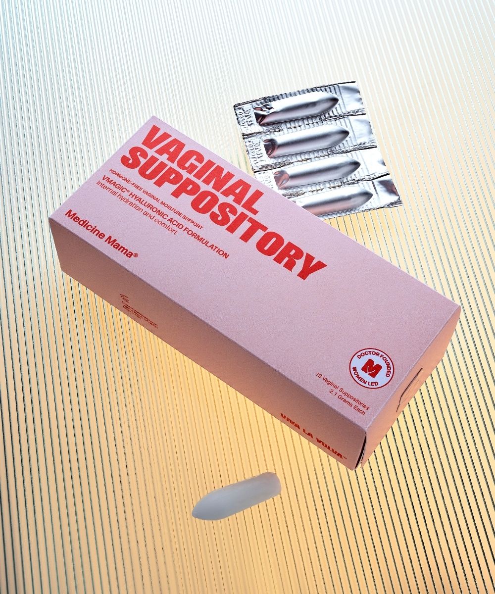 A pink box labeled “Vaginal Suppository” sits on a textured surface, with three foil-wrapped suppositories above it and one unwrapped suppository below.