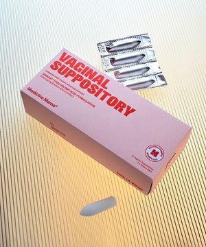 A pink box labeled VMAGIC® Vaginal Suppository for vaginal dryness, with three hyaluronic acid suppositories in foil packs and one unwrapped on a textured, light background.