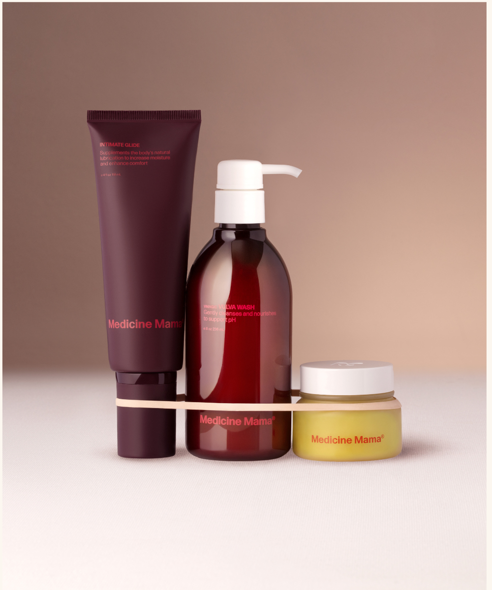 Three Medicine Mama skincare products—a tube, a pump bottle, and a small jar—are arranged together against a neutral background, held by a white band.