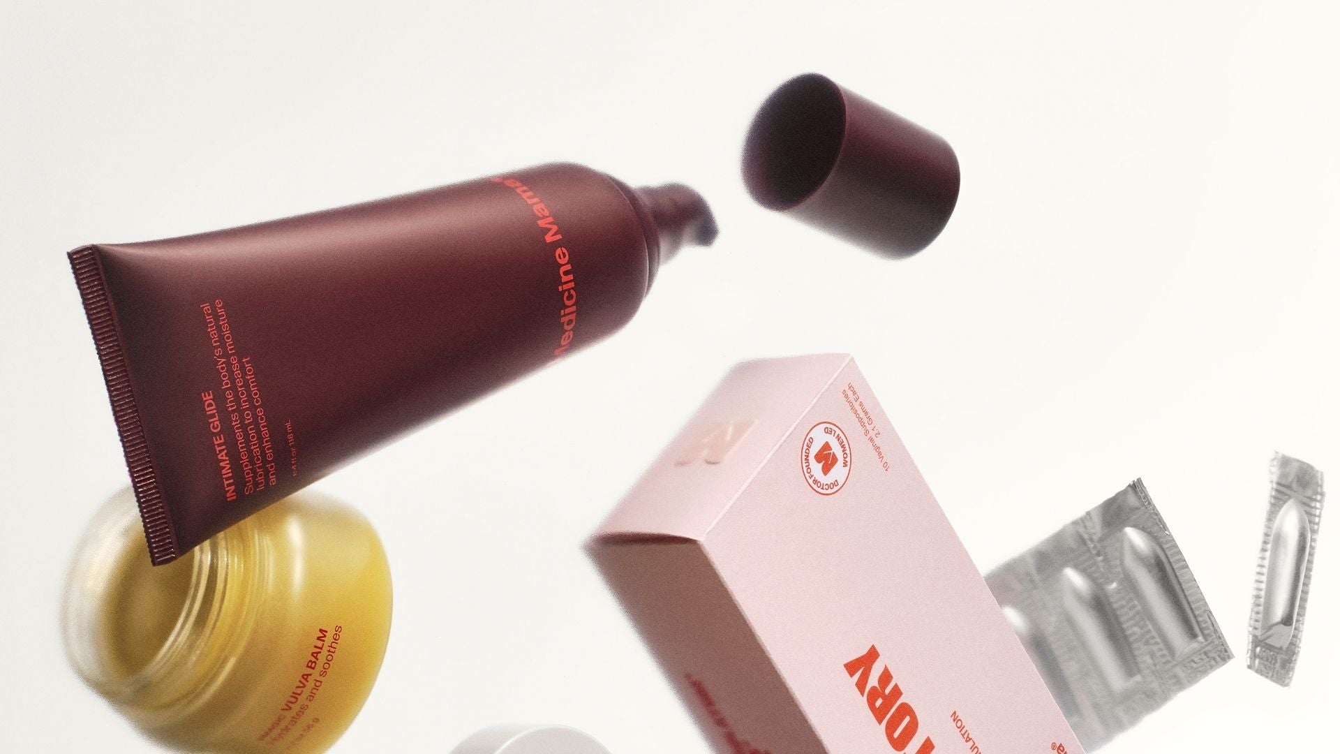 A maroon tube, an open jar with yellow balm, a pink medicine box, and two silver blister packs float against a white background.